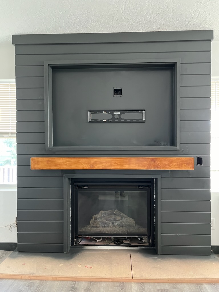 Fireplace surround clad in dark shiplap with a timber mantel