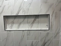Large-format marble-look tiled wall with a recessed shelf