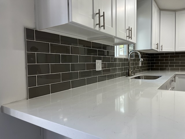 The same kind of kitchen finished, with a grey subway tile backsplash above a light stone counter